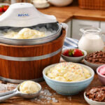 Rival ice cream maker churning vanilla ice cream on a wooden kitchen counter with bowls of toppings in a cozy home kitchen, 16:9 featured image.